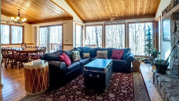A spacious living room with a large wooden ceiling, a black leather sofa with multiple cushions, a patterned rug, and a stone fireplace. - Dancing Bear (Davis)