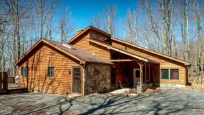 A wooden cabin with a stone foundation, a porch, and a clear view of the surrounding forest. - Dancing Bear (Davis)