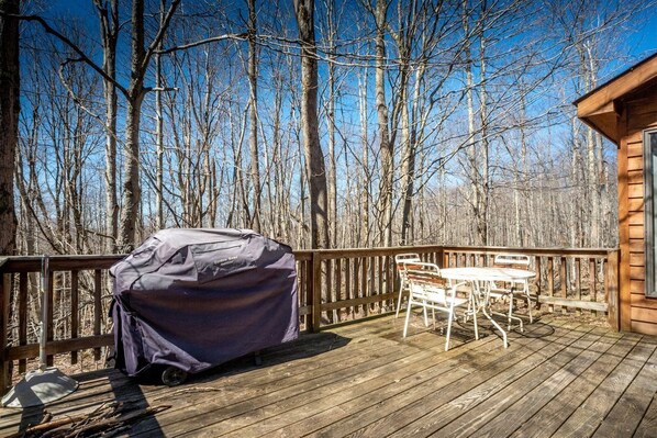 A wooden deck with a covered grill, a table, and chairs.