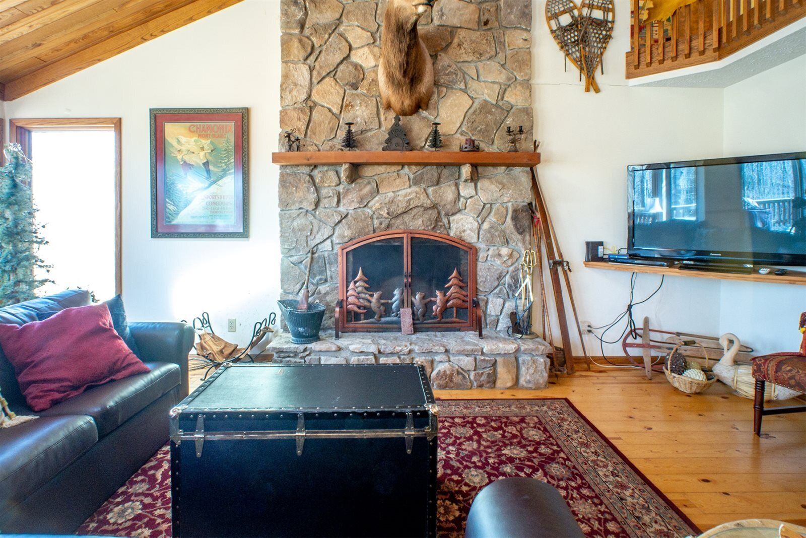 A cozy living room with a stone fireplace, a leather sofa, a television, and a rustic decor.