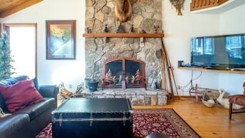 A cozy living room with a stone fireplace, a leather sofa, a television, and a rustic decor.