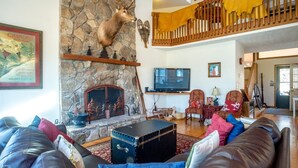 A spacious living room with a stone fireplace, a mounted deer head, a television, and a cozy seating area with leather couches and colorful pillows. - Dancing Bear (Davis)