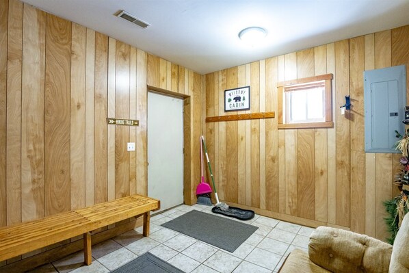 L’intérieur d’un chalet en bois, avec un banc, un panneau indiquant les sentiers de randonnée, une pancarte de bienvenue et un balai appuyé contre le mur.