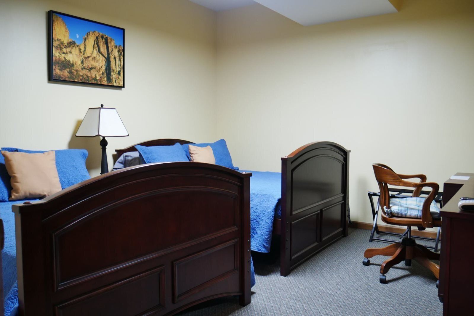 A bedroom with a bed, a desk, a chair, and a painting on the wall.