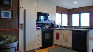 Cocina compacta con armarios blancos, estufa negra, microondas y lavavajillas. Se aprecia una ventana con vistas al exterior.