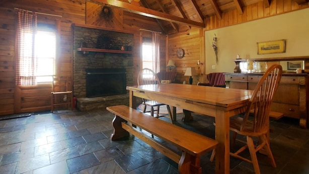 A rustic cabin interior with a stone fireplace, wooden dining table, benches, and a kitchen area with a stove. - Coire Taigh (Davis)