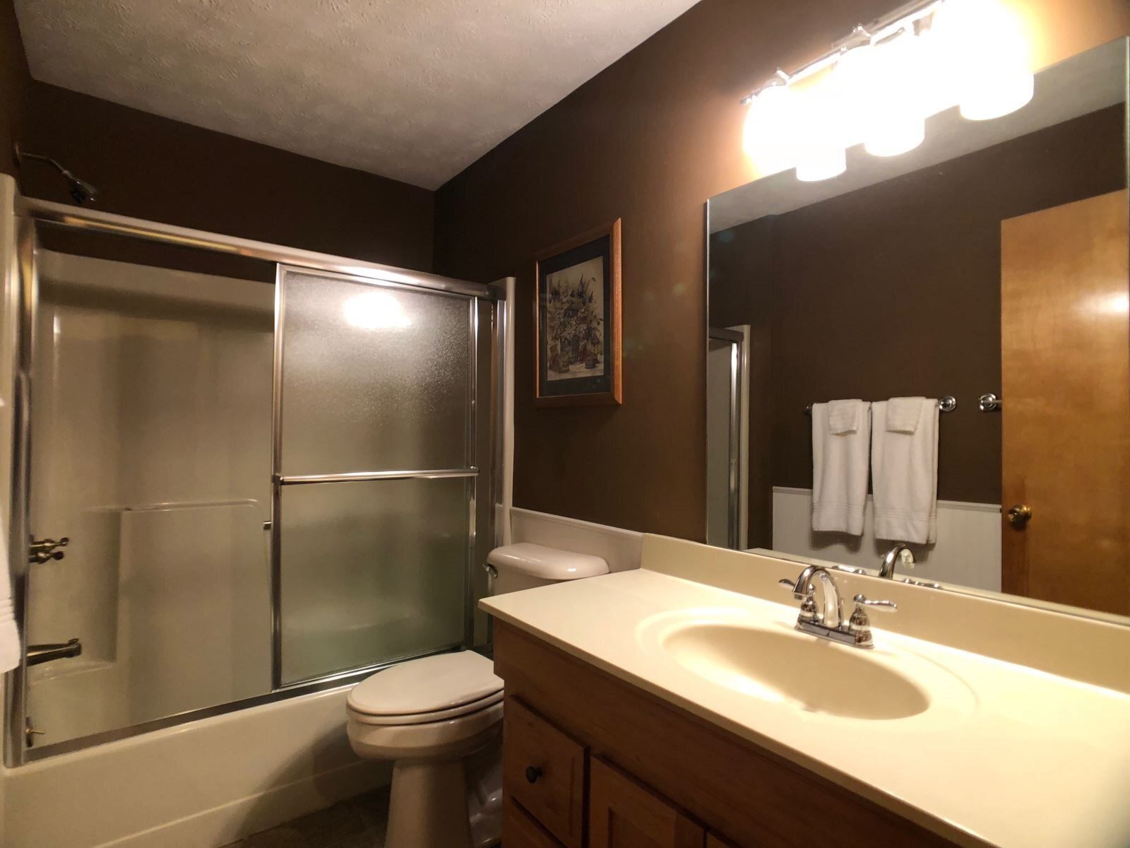 A bathroom with a glass-enclosed shower, a toilet, a sink with a mirror, and a towel rack with towels.