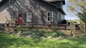 A two-story house with a red door, a covered porch, and a small deck. - Coire Taigh (Davis)