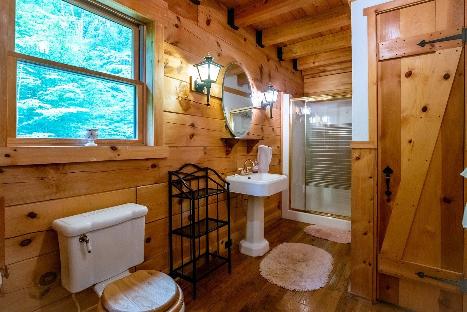 A wooden cabin bathroom with a toilet, sink, and shower.