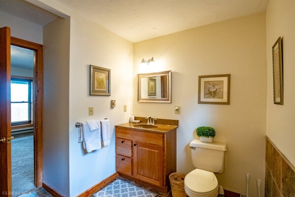 A bathroom with a wooden vanity, a toilet, a sink, and a small potted plant.