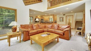 A spacious living room with a large leather sectional sofa, a wooden coffee table, and a view of a forest through a large window. - Chamonix (Davis)