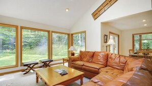 A spacious living room with large windows, a leather sofa, a wooden coffee table, and a dining area with a table and chairs. - Chamonix (Davis)