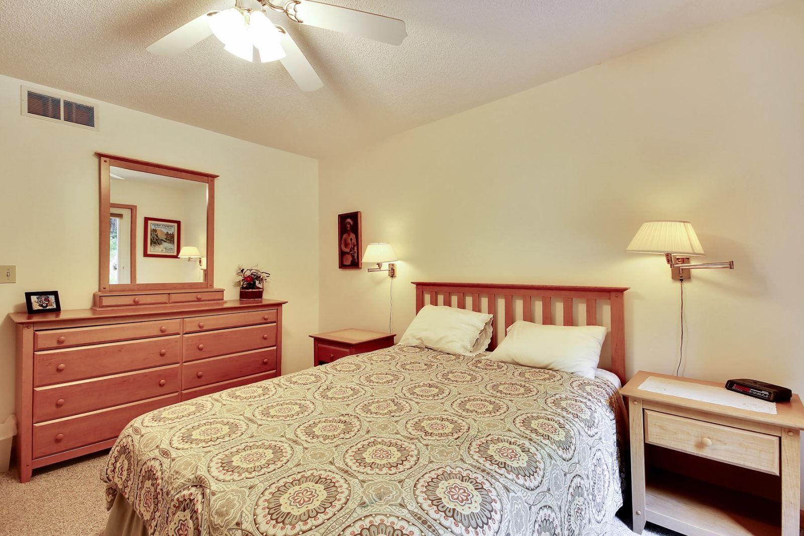 Une chambre à coucher comprenant un lit, une commode, une table de chevet, une lampe et un ventilateur de plafond.