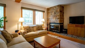 A cozy living room with a stone fireplace, a television on a wooden cabinet, and a beige sofa. - Deerfield Village 106 (Davis)