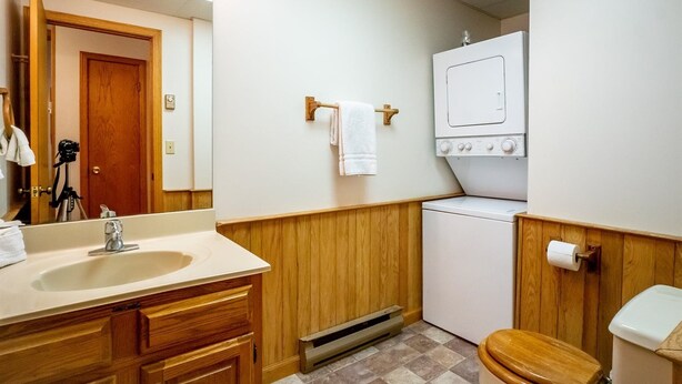 A compact bathroom with a wooden vanity, a sink, a mirror, a toilet, and a washing machine. - Deerfield Village 106 (Davis)