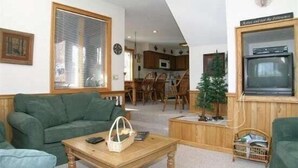 Ein Wohnzimmer mit einem grünen Sofa, einem Holztisch und einem an einer Holzwand montierten Fernseher.