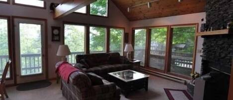 A cozy living room with a fireplace, large windows, and a stone accent wall.