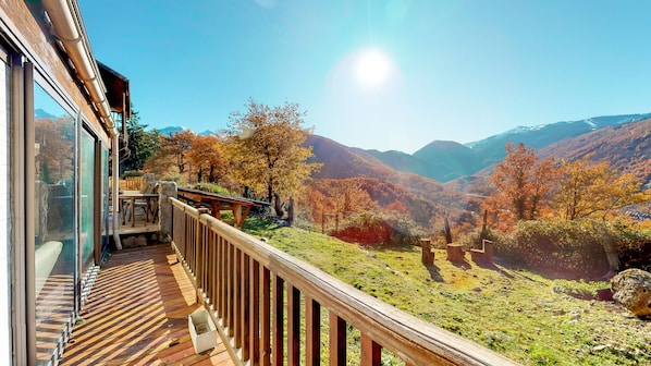 A wooden deck with a glass balustrade overlooking a mountainous landscape with autumn foliage.