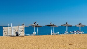 Een strand met parasols en ligstoelen, een kinderwagen, en een helderblauwe lucht.