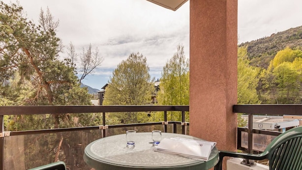 A balcony with a round table, two chairs, and a view of trees and buildings.