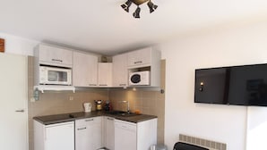 A compact kitchen with white cabinets, a microwave, a coffee maker, and a dining table with chairs.