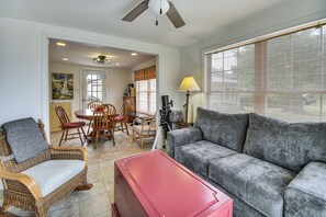 Un salon avec un canapé gris, des fauteuils en osier, un buffet rouge et un coin repas comprenant une table et des chaises.