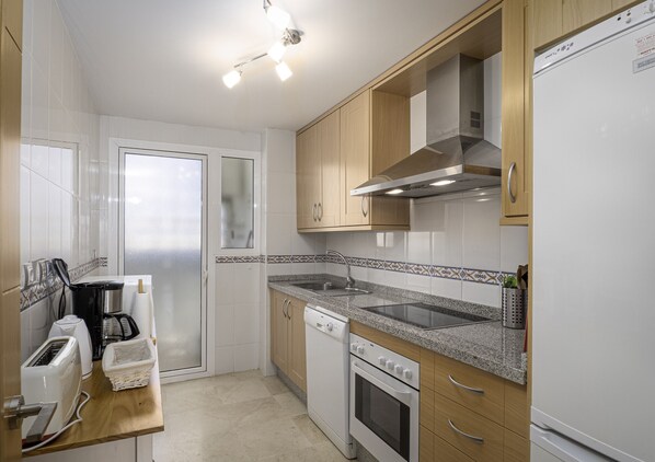 Een moderne keuken met houten kastjes, een granieten aanrechtblad, een inbouwoven, een vaatwasser en een koelkast.