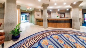 A lobby with a reception desk, large stone columns, and a patterned carpet.