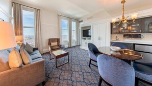 A hotel room with a sofa, armchair, coffee table, dining table, and a TV.