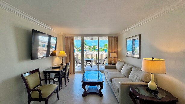 A hotel room with a sofa, chairs, a coffee table, a TV, and a balcony with outdoor furniture. - Marco Beach Ocean Resort 610: Private 1 Bedroom condo; New Tile,TV's (Marco Island)