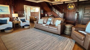 A cozy living room with a brown leather sofa, striped armchairs, and a wooden staircase. - Absolutely fantastic, charming retreat with ocean views! (Seaside)