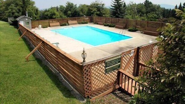 Piscina retangular rodeada por um deck de madeira e cerca de madeira com tela.