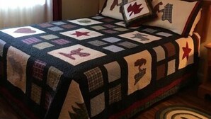 Quarto com colcha acolchoada estampada e cabeceira decorada com almofadas.