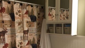 Casa de banho com cortina de chuveiro estampada com motivos de animais, sanita, armário com espaço de armazenamento e toalha pendurada na parede.