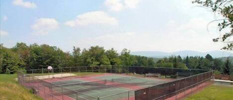 An outdoor tennis court surrounded by trees and a grassy area.