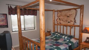 A four-poster bed with a quilt, a mounted animal hide, a television, and a window with blinds. - Beaver Ridge 260 (Davis)