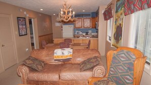 A living room with a brown leather sofa, patterned armchair, and a chandelier. - Beaver Ridge 260 (Davis)