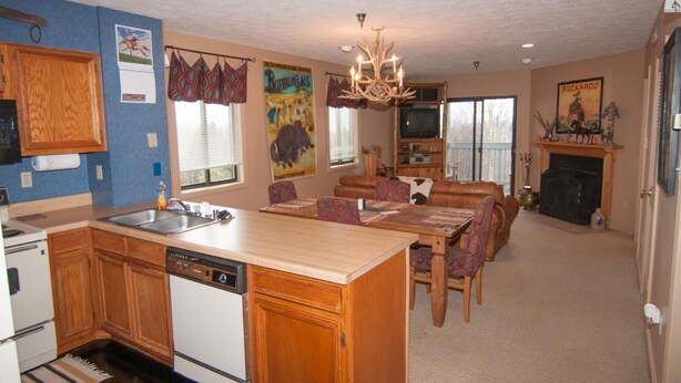 A spacious kitchen with wooden cabinets, a dishwasher, and a dining area with a large island and patterned chairs. - Beaver Ridge 260 (Davis)