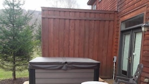 A hot tub on a wooden deck with a wooden fence and a rocking chair in the background. - Aspen Village 35 (Davis)