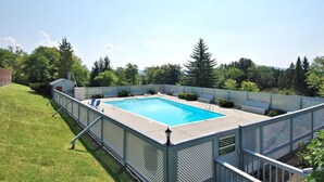 Ein rechteckiger Pool mit Metallzaun, umgeben von Rasenfläche und Bäumen.