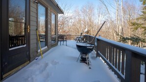 Una terrazza riparata con una griglia barbecue e mobili da esterno, circondata da neve e alberi.