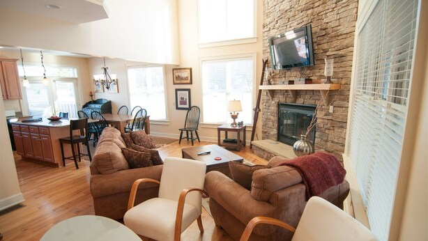 A spacious living room with a stone fireplace, a television mounted on the wall, and a cozy seating area with a sofa and chairs.