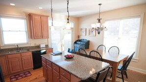 A kitchen with wooden cabinets, granite countertops, a dining table with chairs, a chandelier, and a window with blinds.