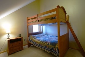 A bunk bed with a wooden frame, a bedside table with drawers, and a lamp. - Bear`s Den (Davis)