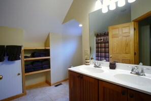 A bathroom with two sinks, a mirror, a towel rack, and a shelf with folded towels. - Bear`s Den (Davis)