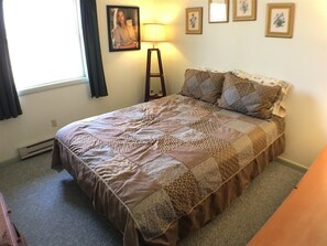 A neatly made bed with a patterned bedspread, a bedside lamp, and a framed picture on the wall. - 5 Acre Wood (Davis)
