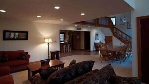 A spacious living room with a red couch, a coffee table, and a patterned sofa. A dining area with a wooden table and chairs is visible in the background. - Almost Heaven (Davis)