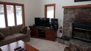 A living room with a stone fireplace, a television on a wooden stand, and a sofa. - Almost Heaven (Davis)