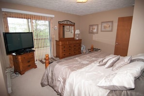 Un dormitorio con cama, cómoda, televisor y ventana con persianas.