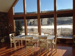 A dining area with a table and chairs, large windows, and a view of a snowy landscape. - Alpen View (Davis)